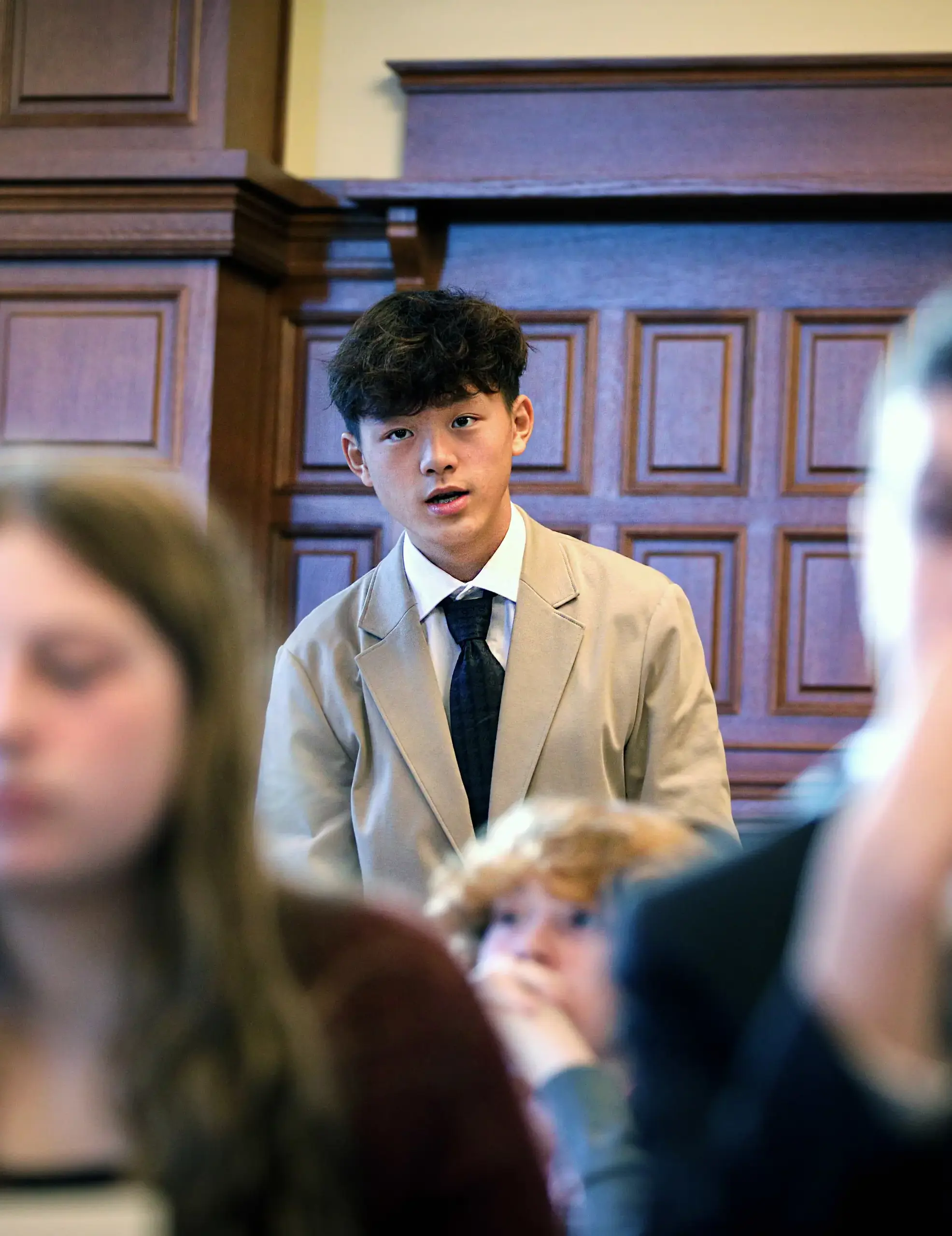 Student in a tan jacket standing and speaking