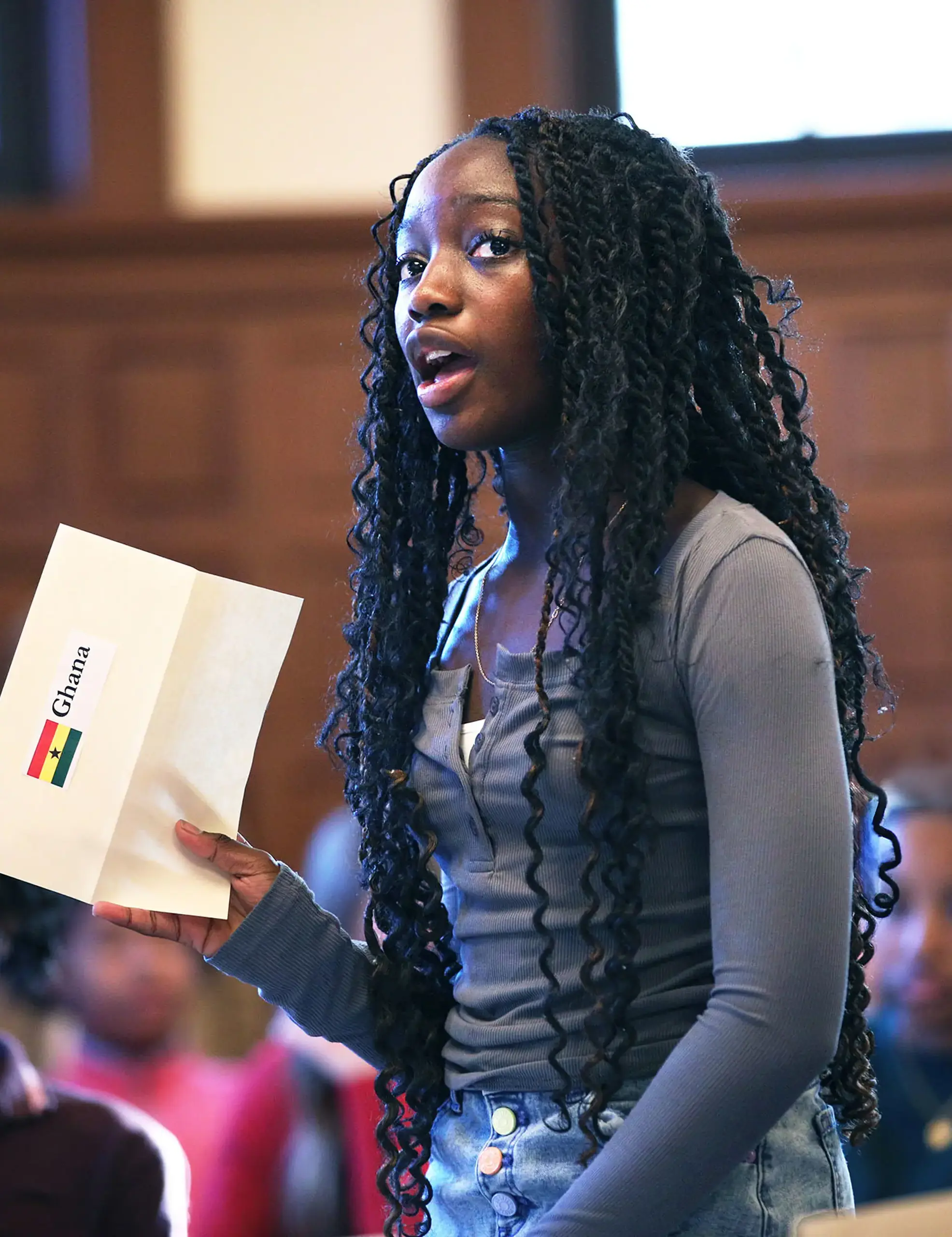 Middle School Student speaking and holding a paper with the Ghana flag. 