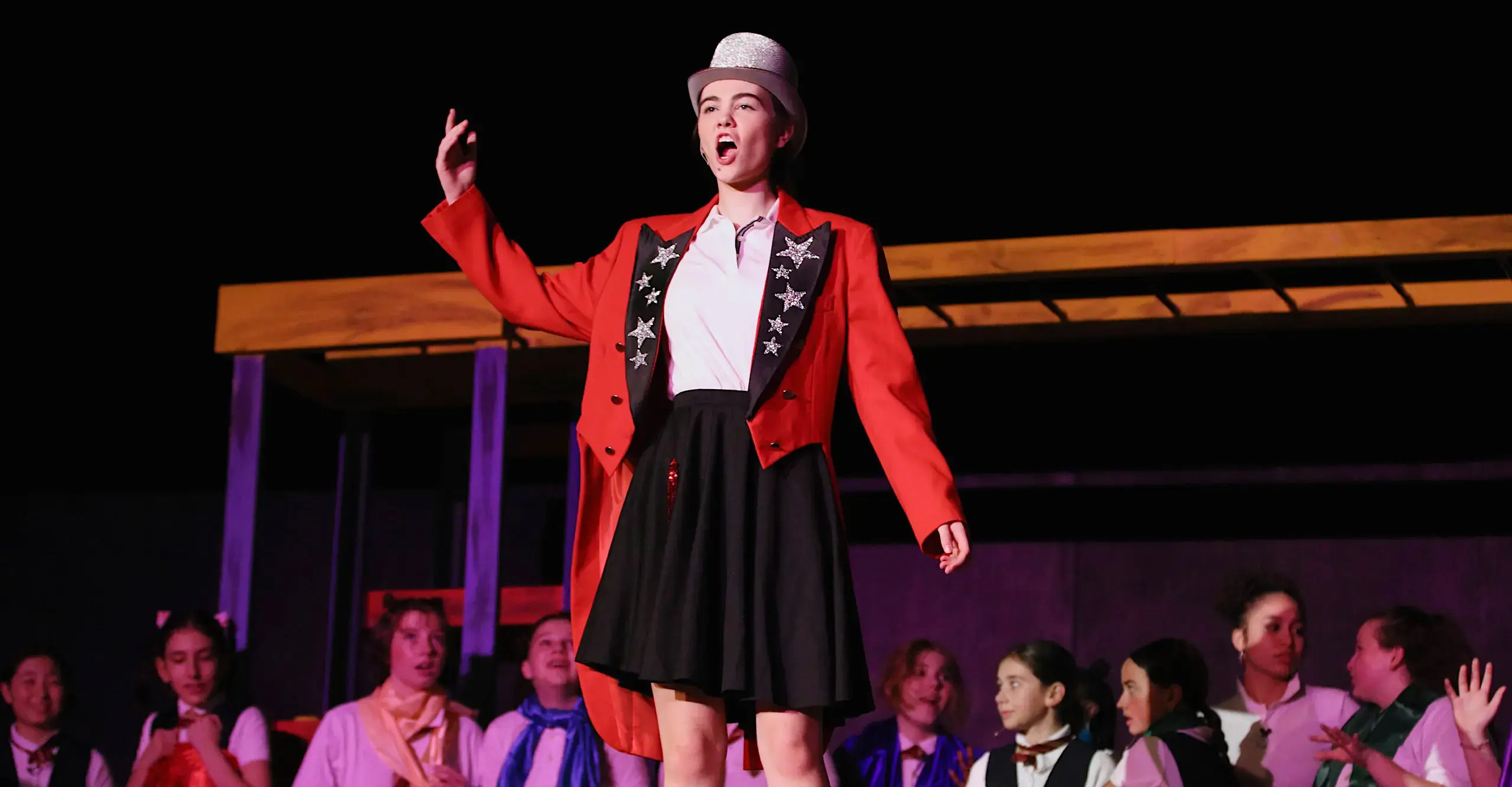 Student actor on stage with top hat from Upper and Middle School performance of Matilda, 2024.