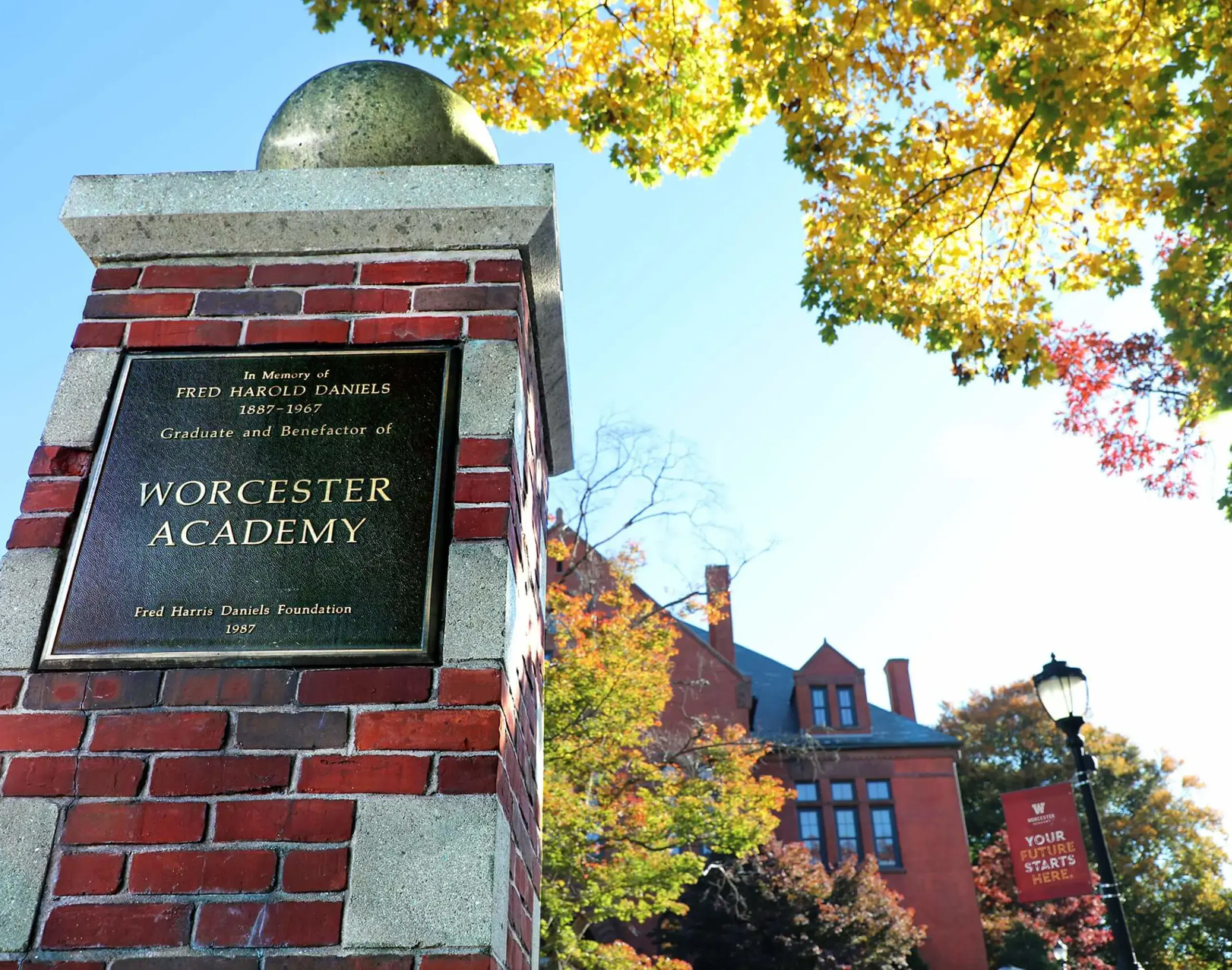 Worcester Academy campus pillar with plaque and 'your future starts here' banner.