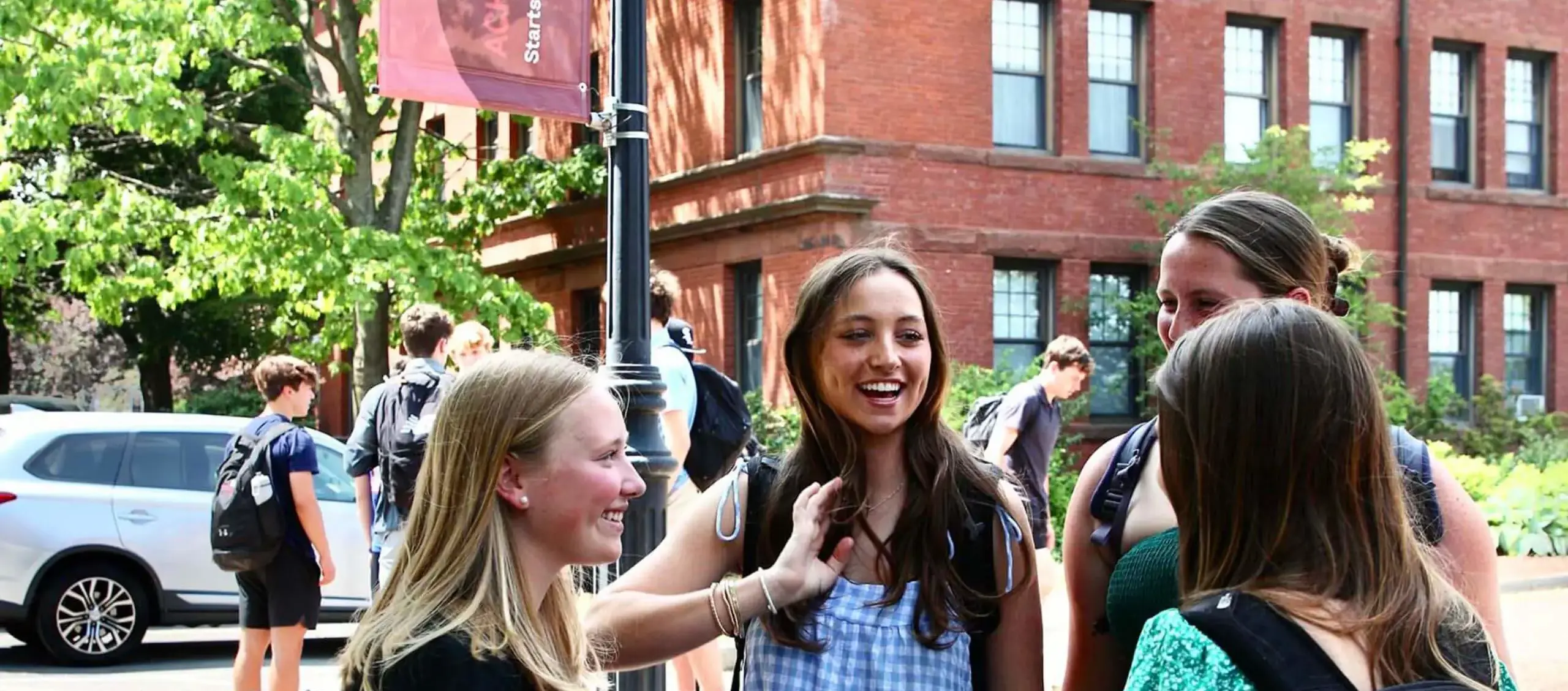 Worcester Academy Middle School students smiling together outside in the sunshine with school buildings in background.