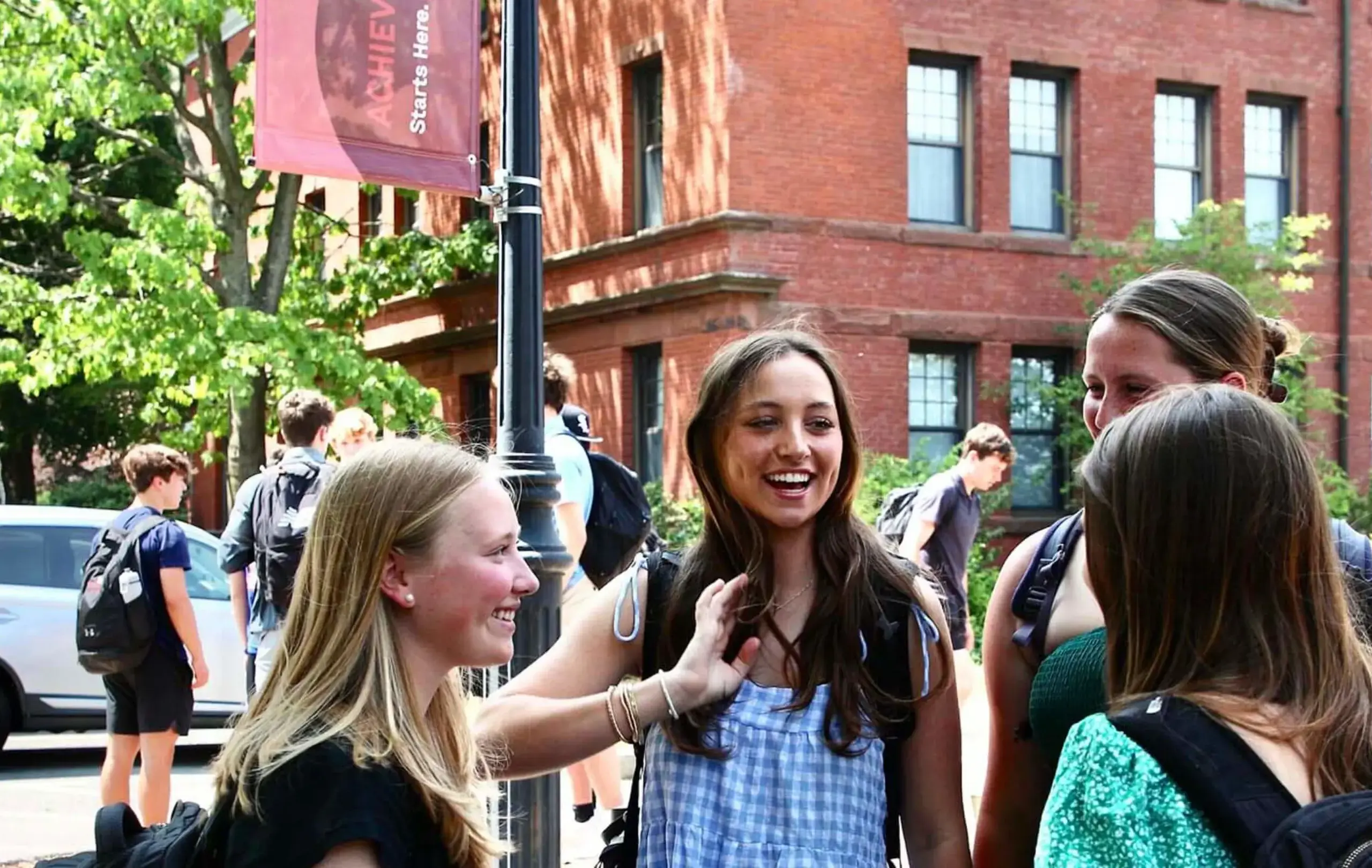 Worcester Academy Middle School students smiling together outside in the sunshine with school buildings in background.