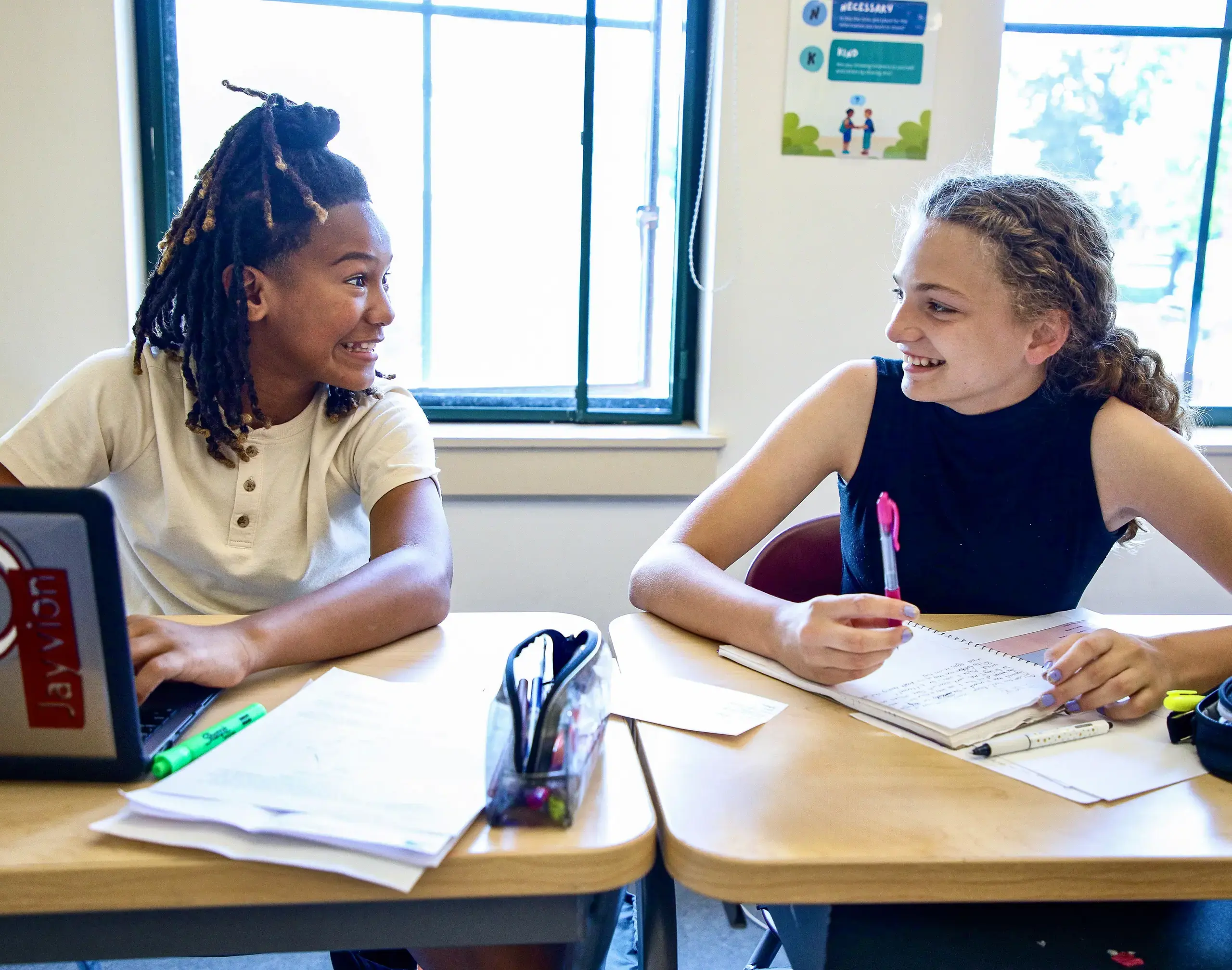 Two Middle School students at their desks smiling.